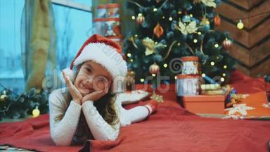 圣诞老人的孩子躺在圣诞树下的红毯子上，把她的头从一边移动到另一边，把手放在上面